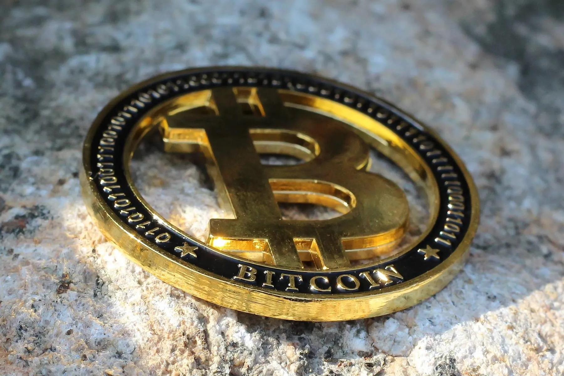 A gold-coloured bitcoin token resting on stone