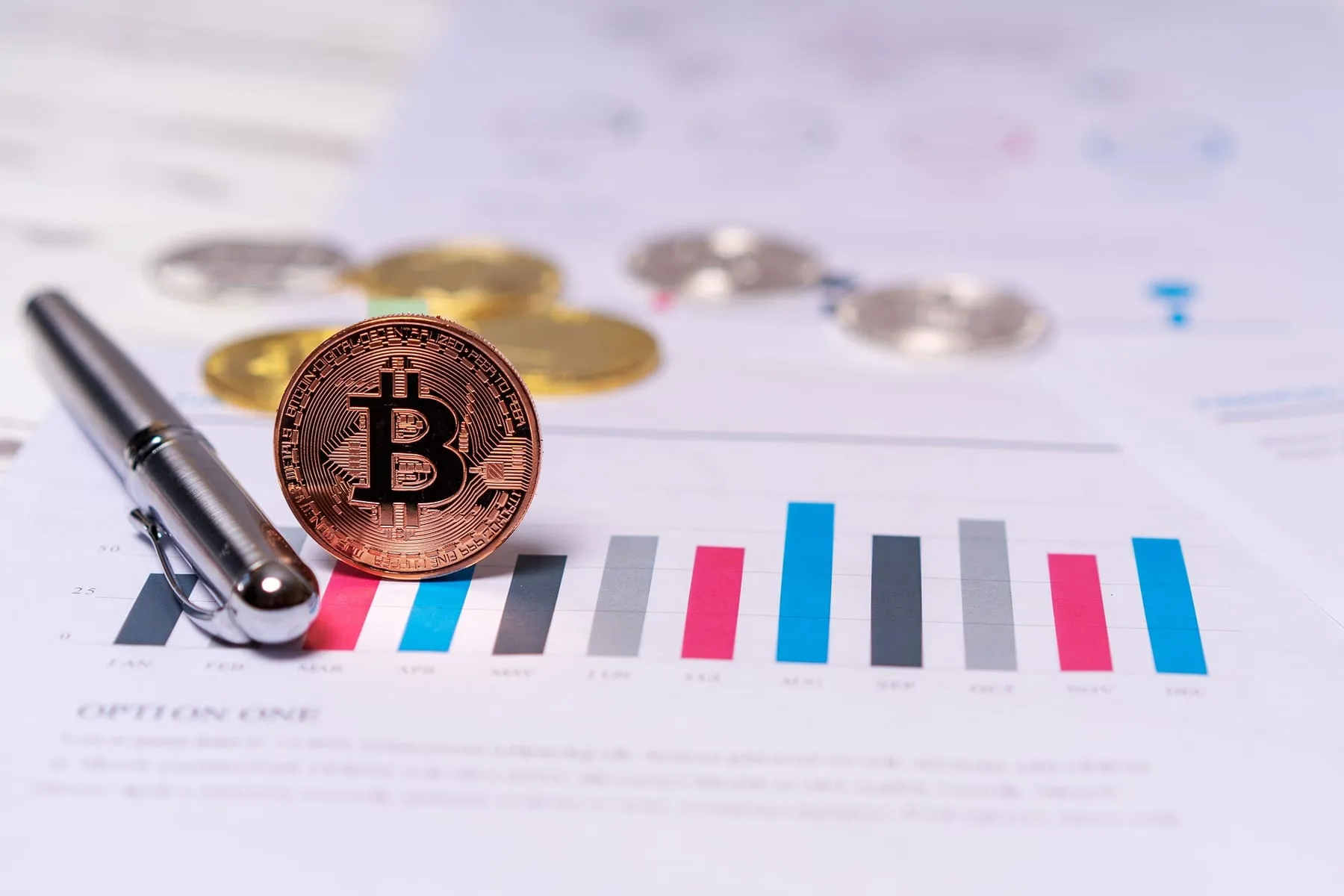 A bitcoin token standing on a printed bar chart report