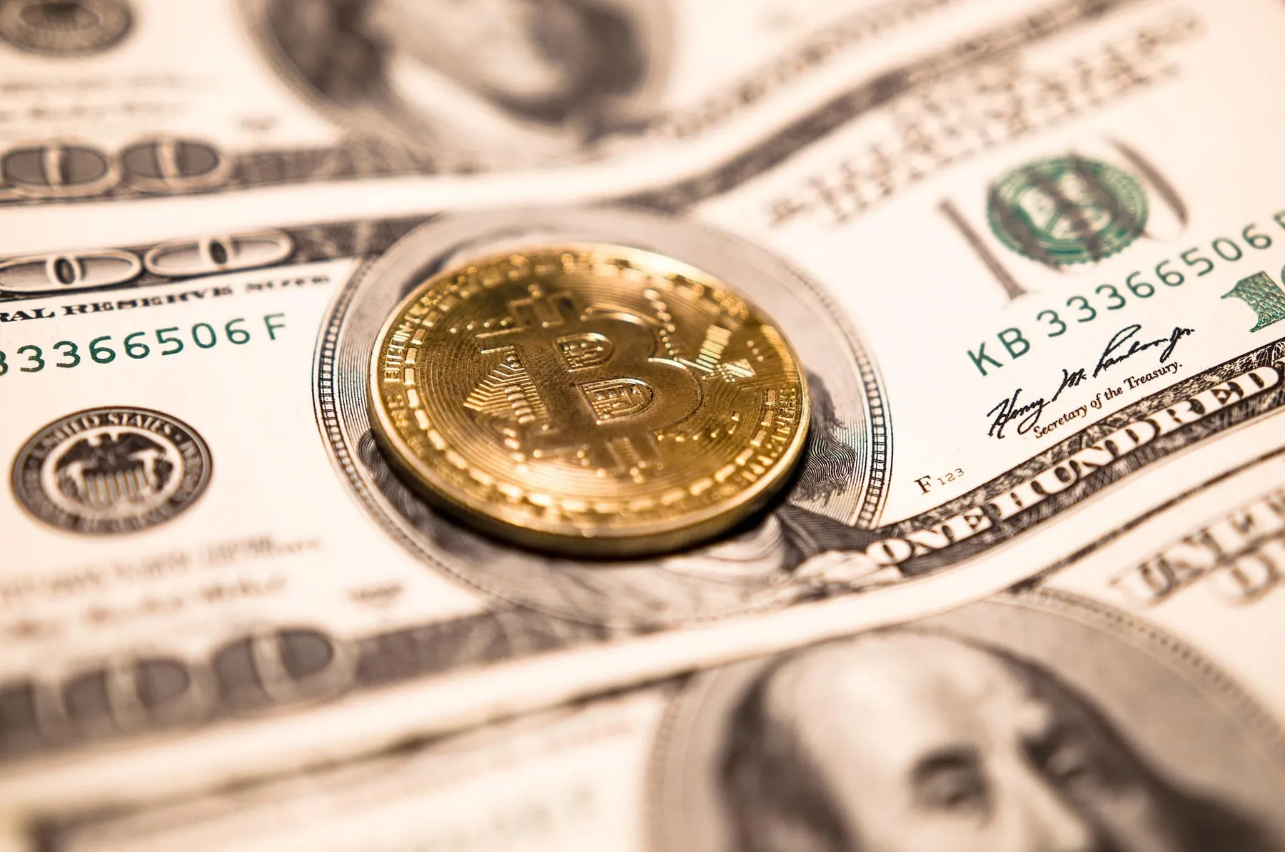 A bitcoin token lying on United States hundred-dollar bills