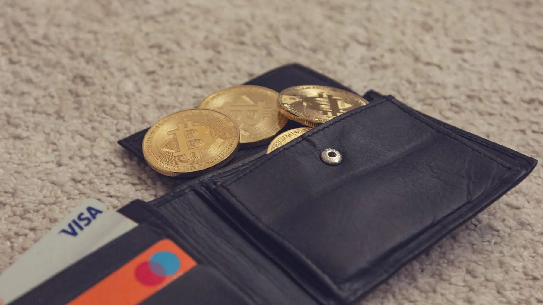 Bitcoin tokens tucked into a leather billfold beside bank cards